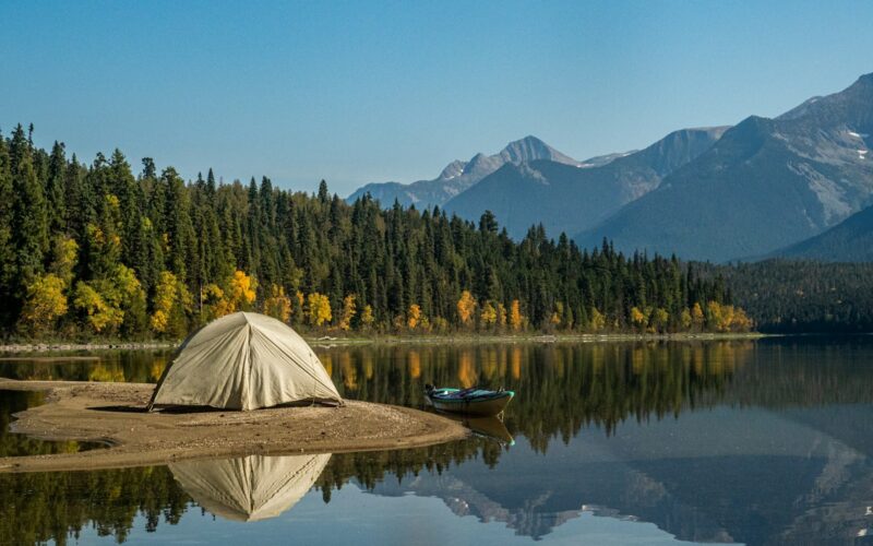 white tent on lake near green trees and mountain under blue sky during daytime