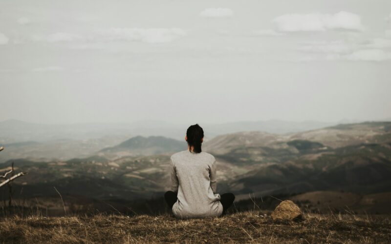 woman sitting on cliff overlooking mountains during daytime
